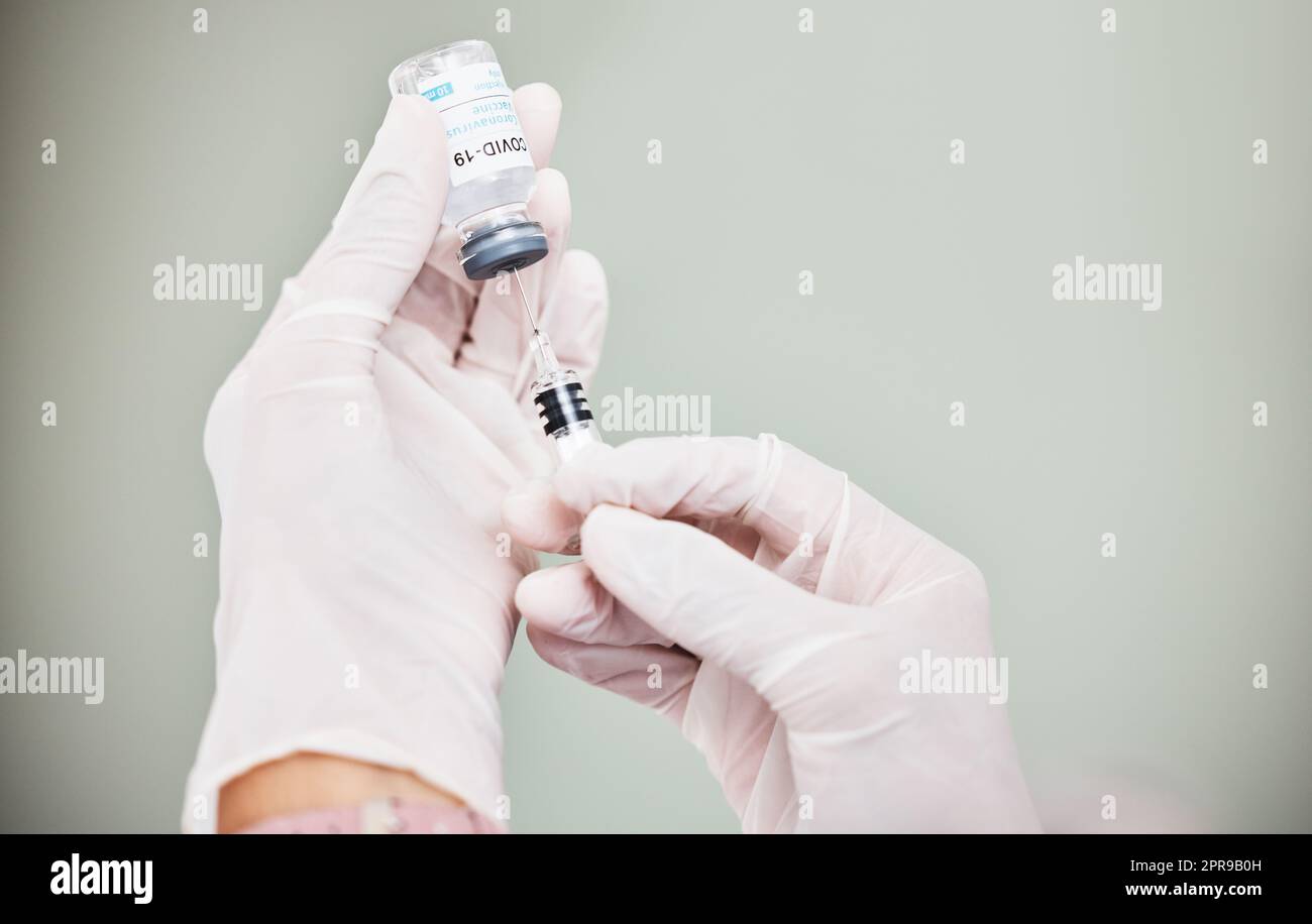 Un scienziato che estrae il farmaco usando una siringa da una fiala con COVID-19 su di essa. Foto Stock