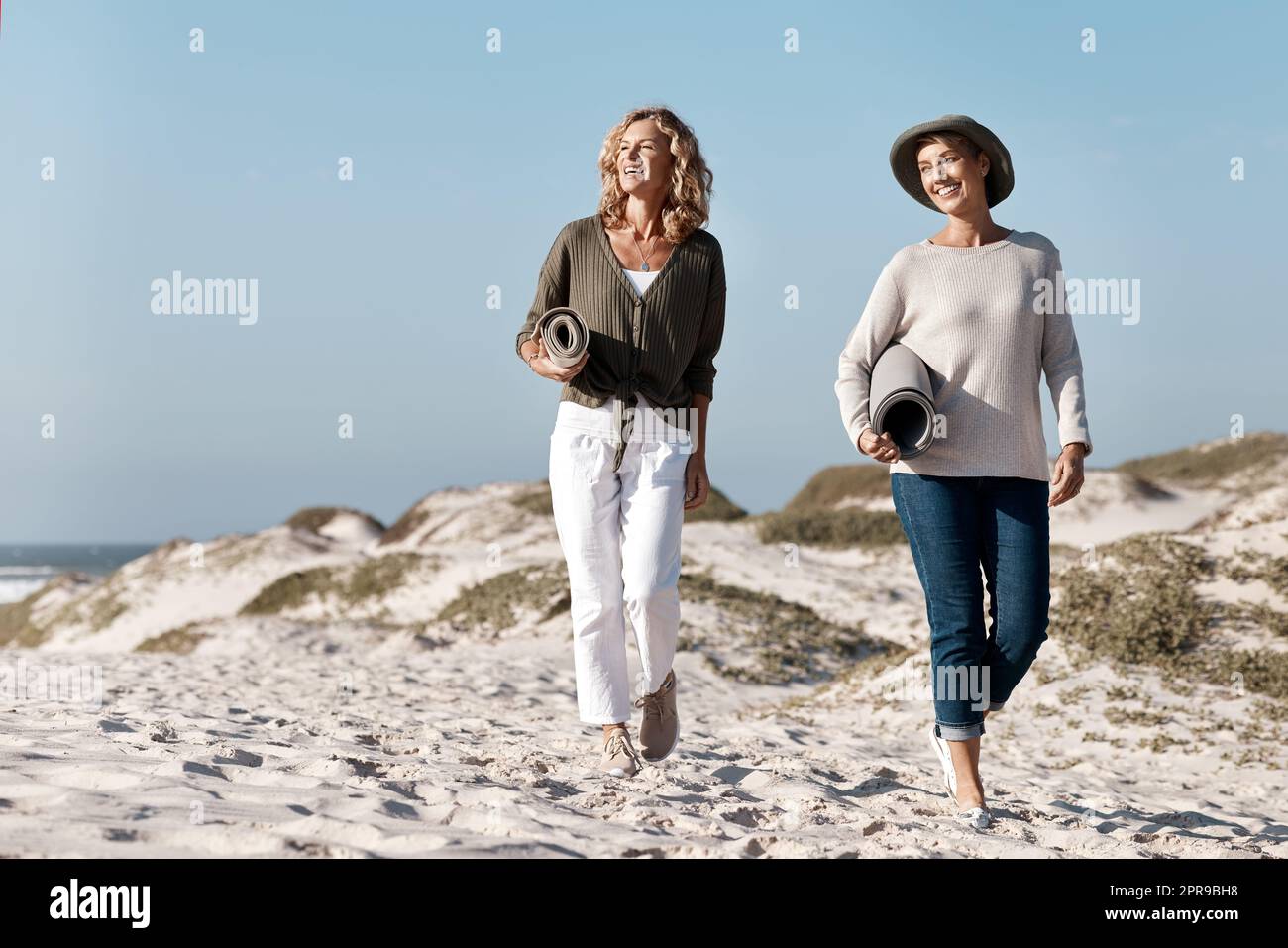È il giorno perfetto per una gita in spiaggia. Scatto a tutta lunghezza di due belle donne mature che camminano con loro sulla spiaggia. Foto Stock