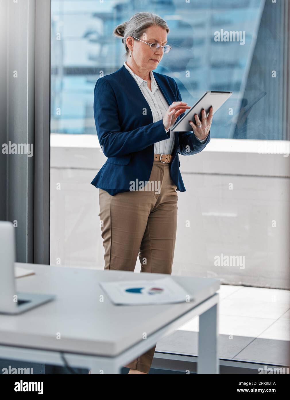 Controllare i progressi dei miei team. Una donna d'affari matura in piedi da sola in ufficio e utilizzando un tablet digitale. Foto Stock