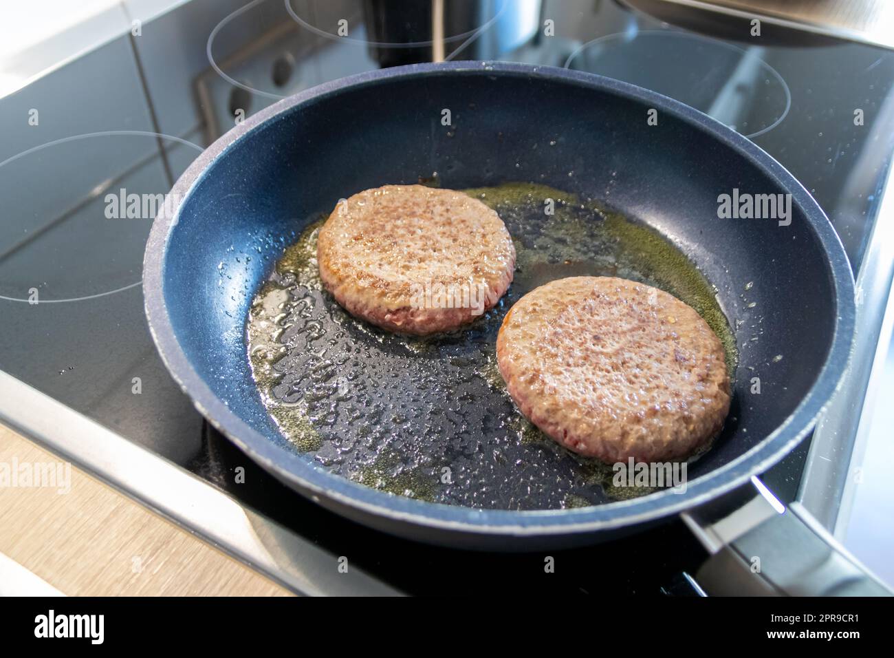 Due hamburger polpettine di carne di hamburger sfrigolante in padella calda con grassi e olio, come deliziosi hamburger fatti in casa polpette al barbecue come cibo veloce malsano pranzo con molte calorie e colesterolo in padella Foto Stock