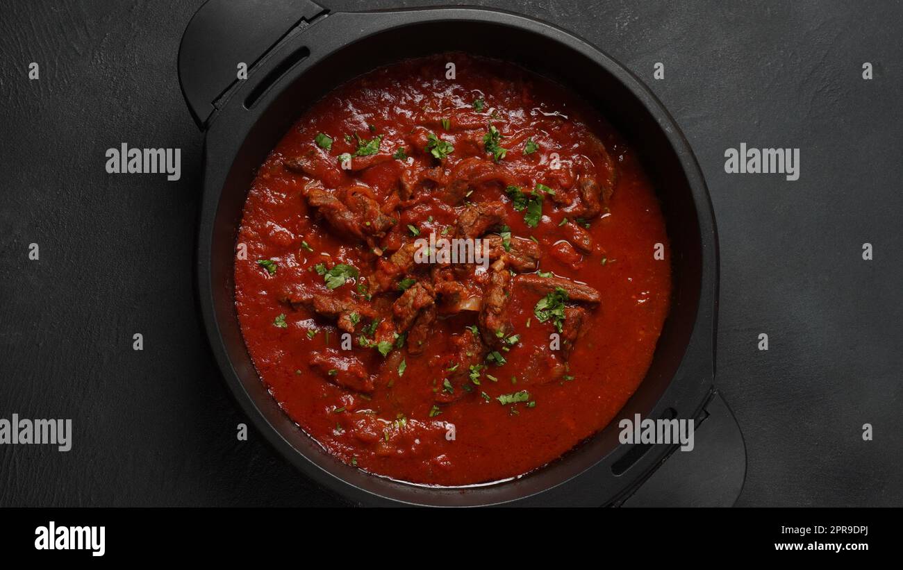 Stufato di manzo con salsa di pomodoro, spezie ed erbe in una padella Foto Stock