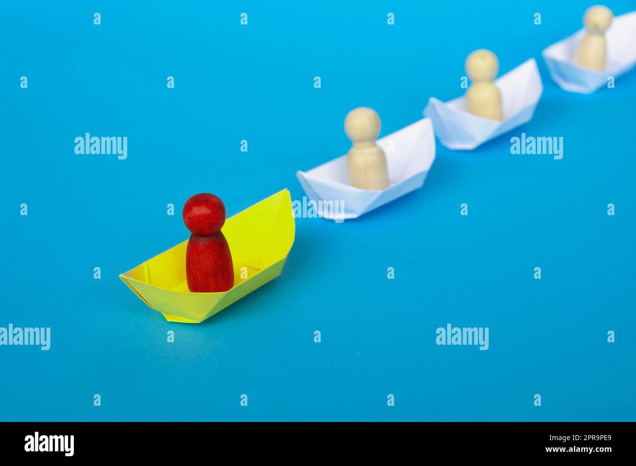 Concetto di leadership - figura di legno rossa su origami di carta gialla che guida il resto della figura su una nave di carta bianca. Foto Stock