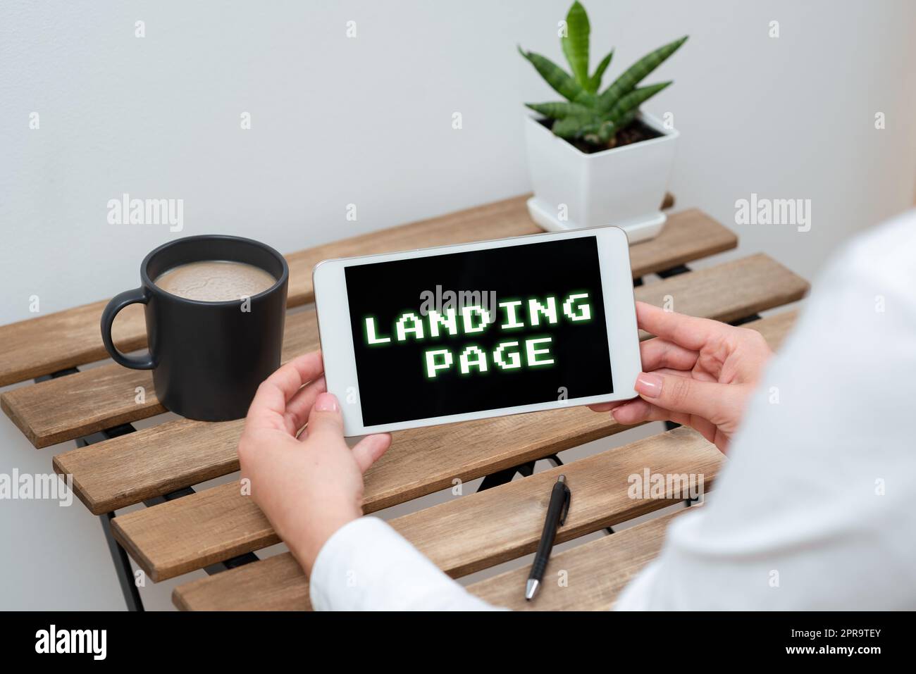 Landing Page con didascalia concettuale. Word per il sito Web accessibile facendo clic su un link in un'altra pagina Web donna che detiene un tablet con dati recenti sulla tabella con caffè, penna e impianto Foto Stock