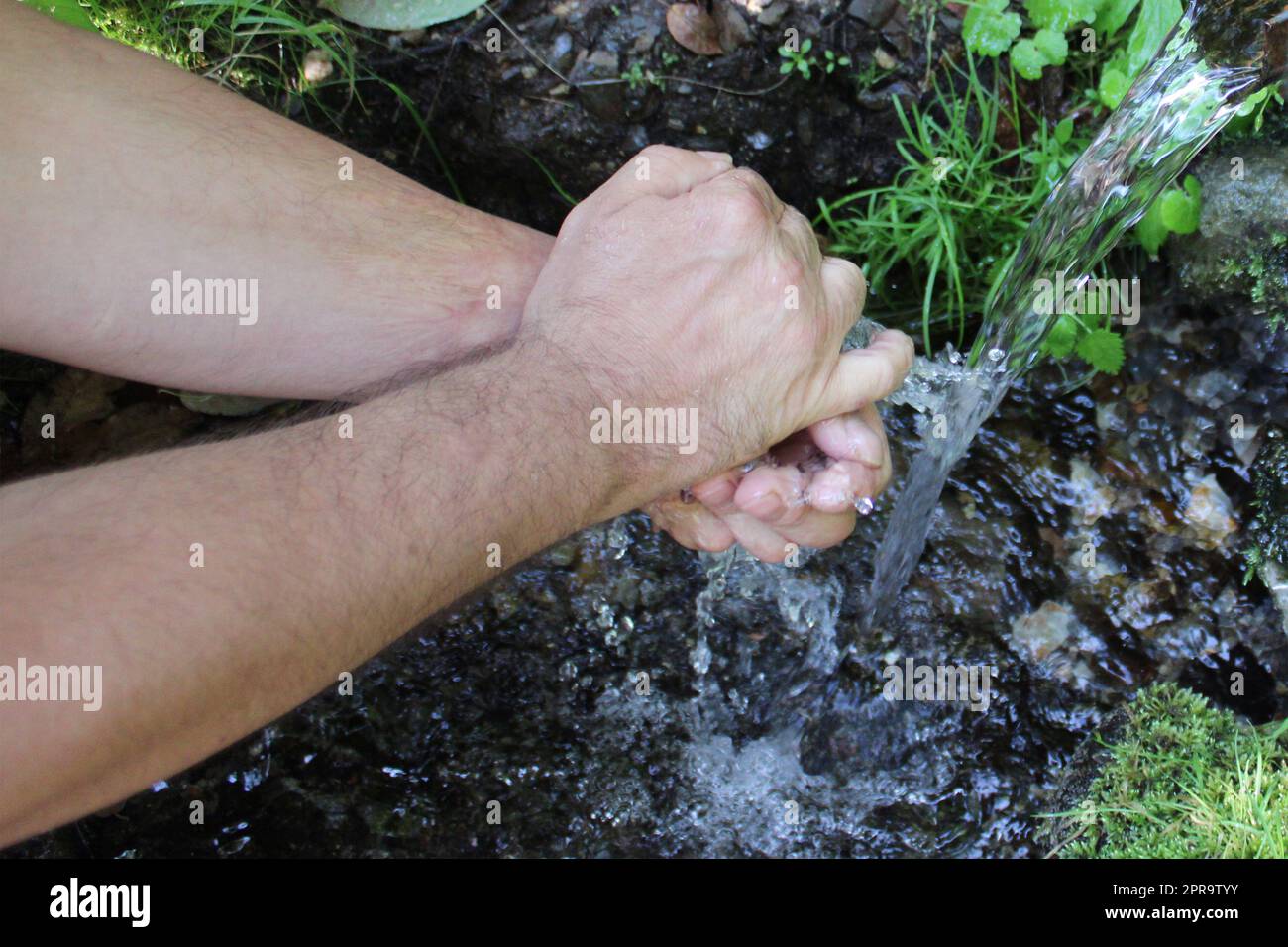 Un uomo si lava le mani in una sorgente nella foresta. Sfondo naturale sfocato Foto Stock