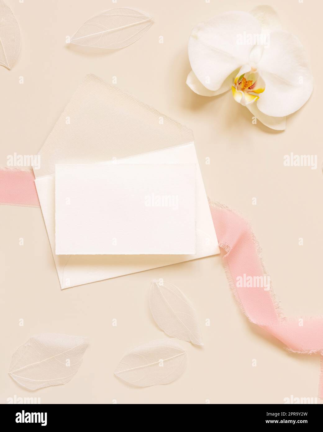 Tessera nuziale su busta vicino a fiori di orchidee bianchi e nastri di seta su un modello giallo Foto Stock