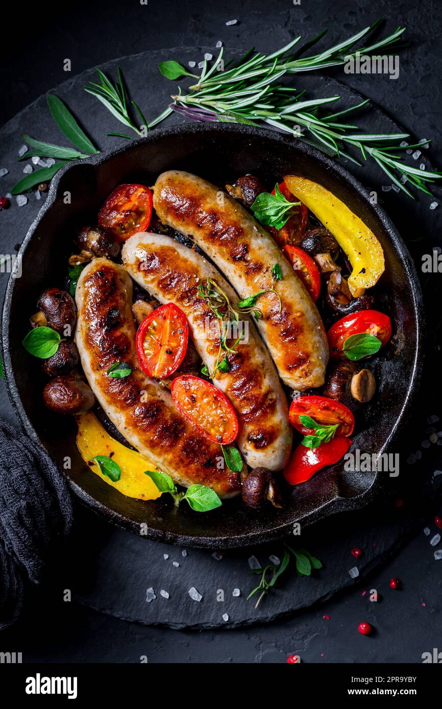 Salsicce e verdure grigliate con erbe in padella di ferro Foto Stock