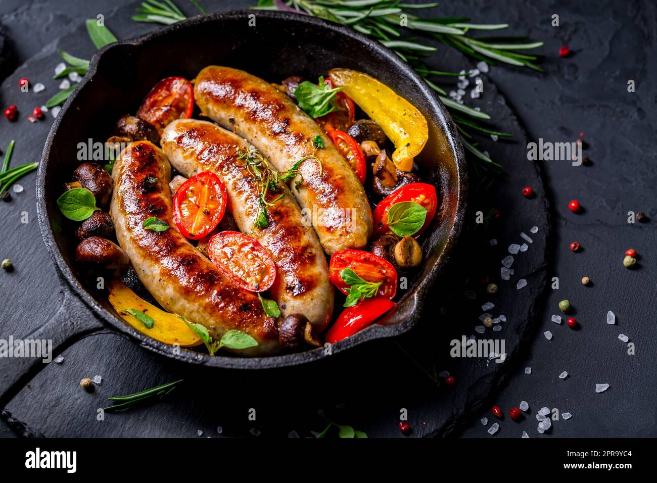 Salsicce e verdure grigliate con erbe in padella di ferro Foto Stock
