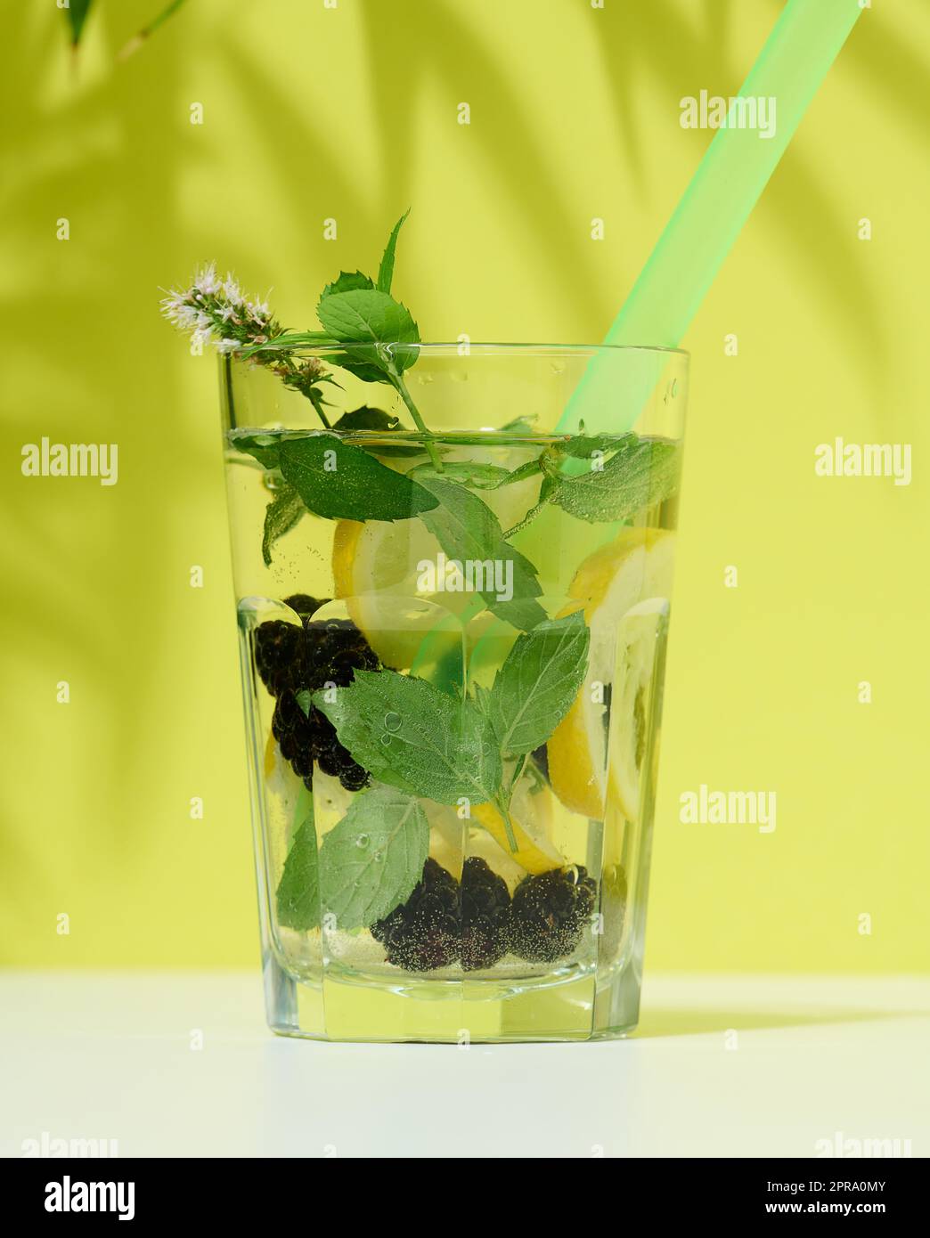 Vetro trasparente con limonata, foglie di menta, fettine di limone e more al centro. Sfondo verde Foto Stock