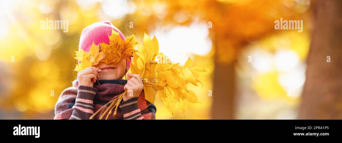 Felice bambino che nasconde gli occhi dietro le foglie d'acero. Foto Stock