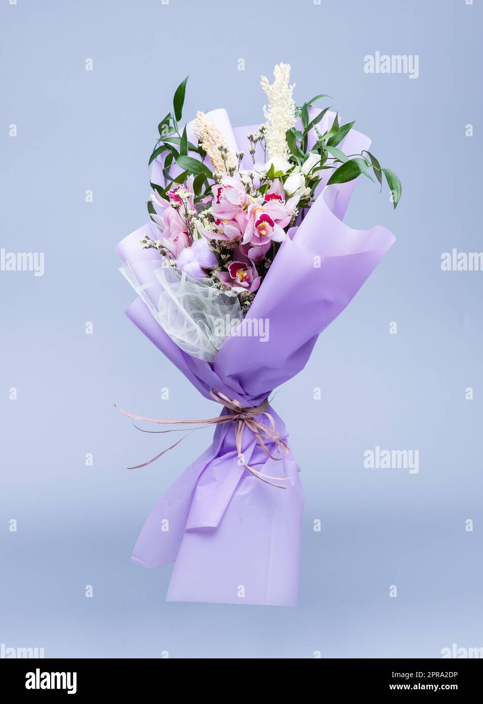 Bouquet di fiori naturali avvolti in carta da traforo floreale si trova in un vaso su sfondo blu. Foto Stock