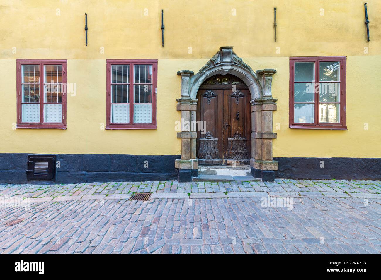 Porta decorata in legno incorniciata da una struttura in pietra, finestre in legno battuto in ferro con pareti gialle e pavimento in ciottoli Foto Stock