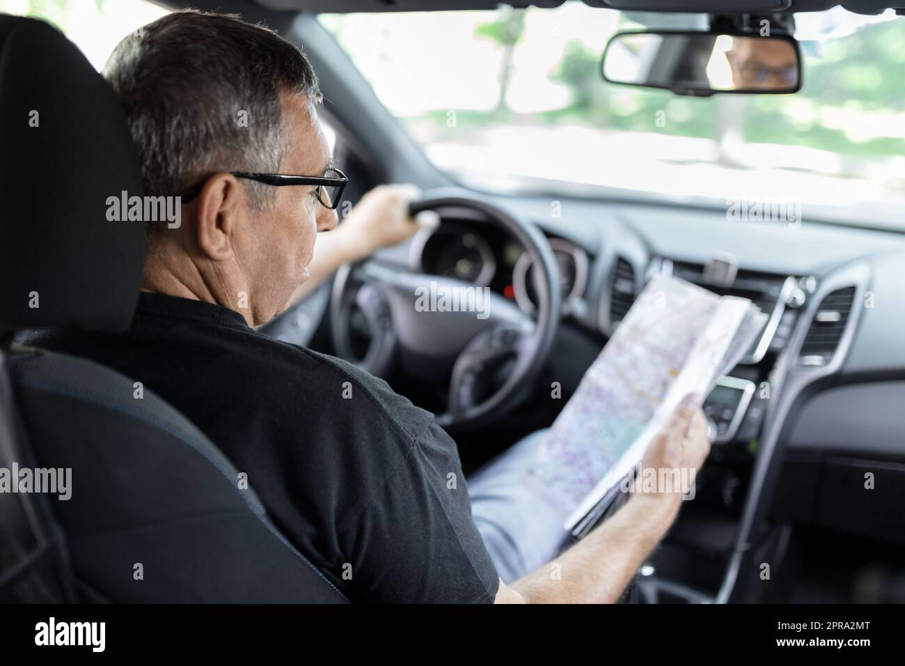 Senior dietro il volante guardando la mappa per le indicazioni Foto Stock