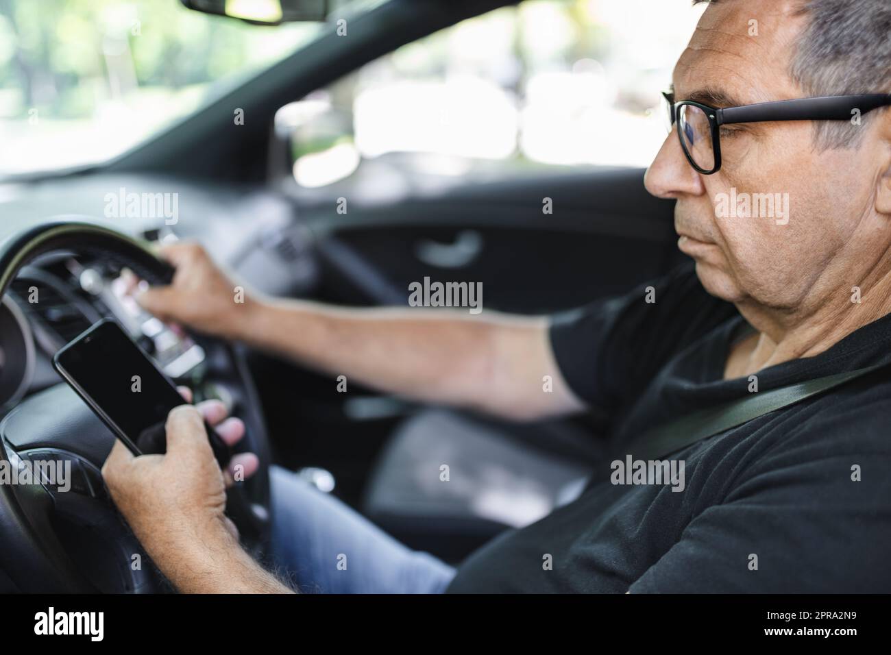 Senior di 70 anni alla guida di un'auto e usando il suo cellulare Foto Stock
