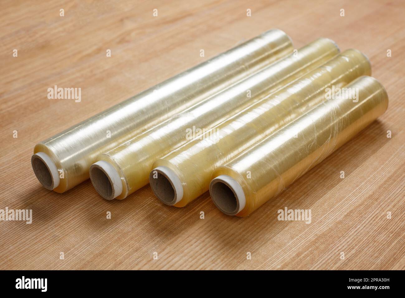 In primo piano su un tavolo di legno si trovano quattro rotoli di pellicola  trasparente per alimenti su una bobina di cartone Foto stock - Alamy