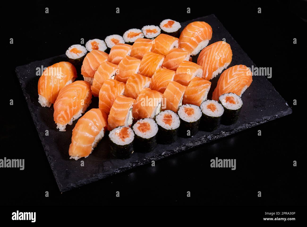 Grande set di rotoli di sashimi con salmone, panini California e Maki su una tavola piatta nera. Foto Stock