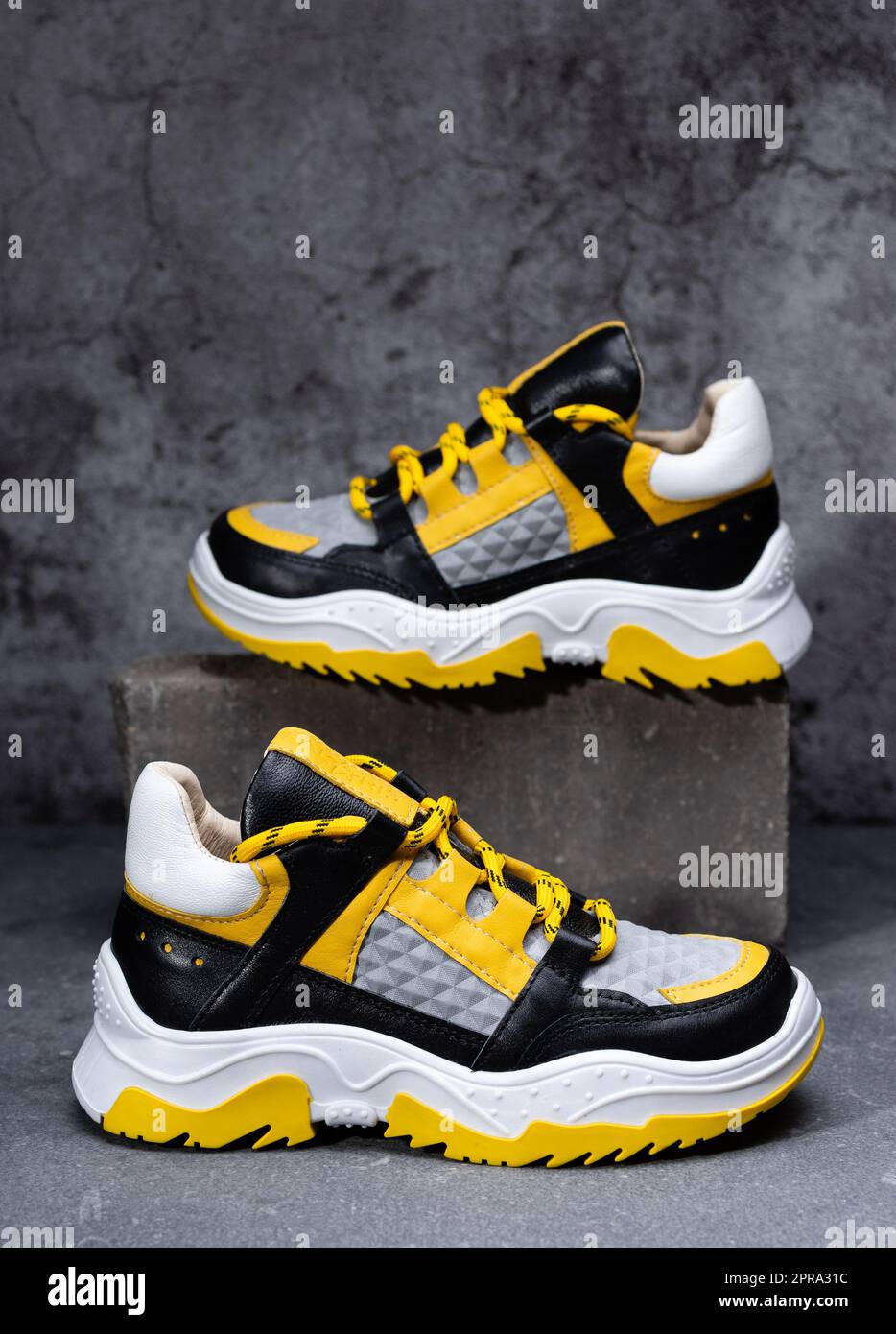Paio di sneaker eleganti e luminose in giallo, nero e bianco su sfondo di cemento grigio. Foto Stock