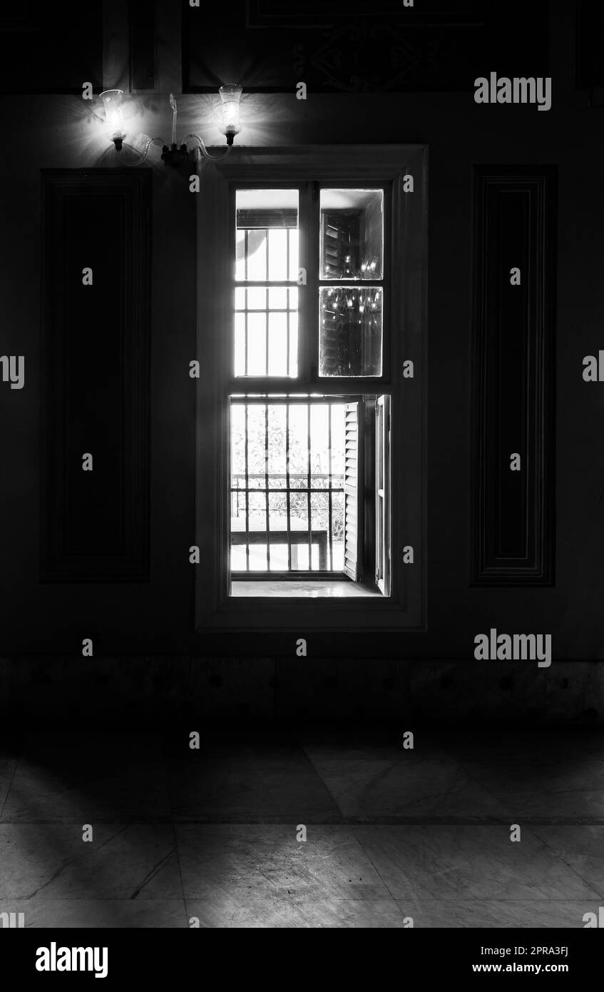 Bianco e nero di finestre strette, che rivelano una luce forte in una stanza buia con pavimento piastrellato in marmo Foto Stock