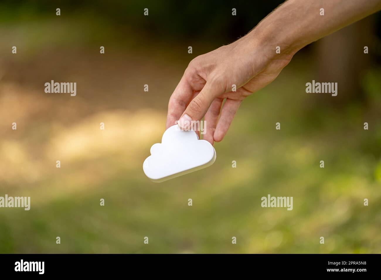 Uomo che tiene in mano un semplice simbolo di nuvola bianca, accesso ai servizi di cloud computing e storage tenuto in mano, isolamento degli oggetti, sfondo sfocato, copy spa Foto Stock