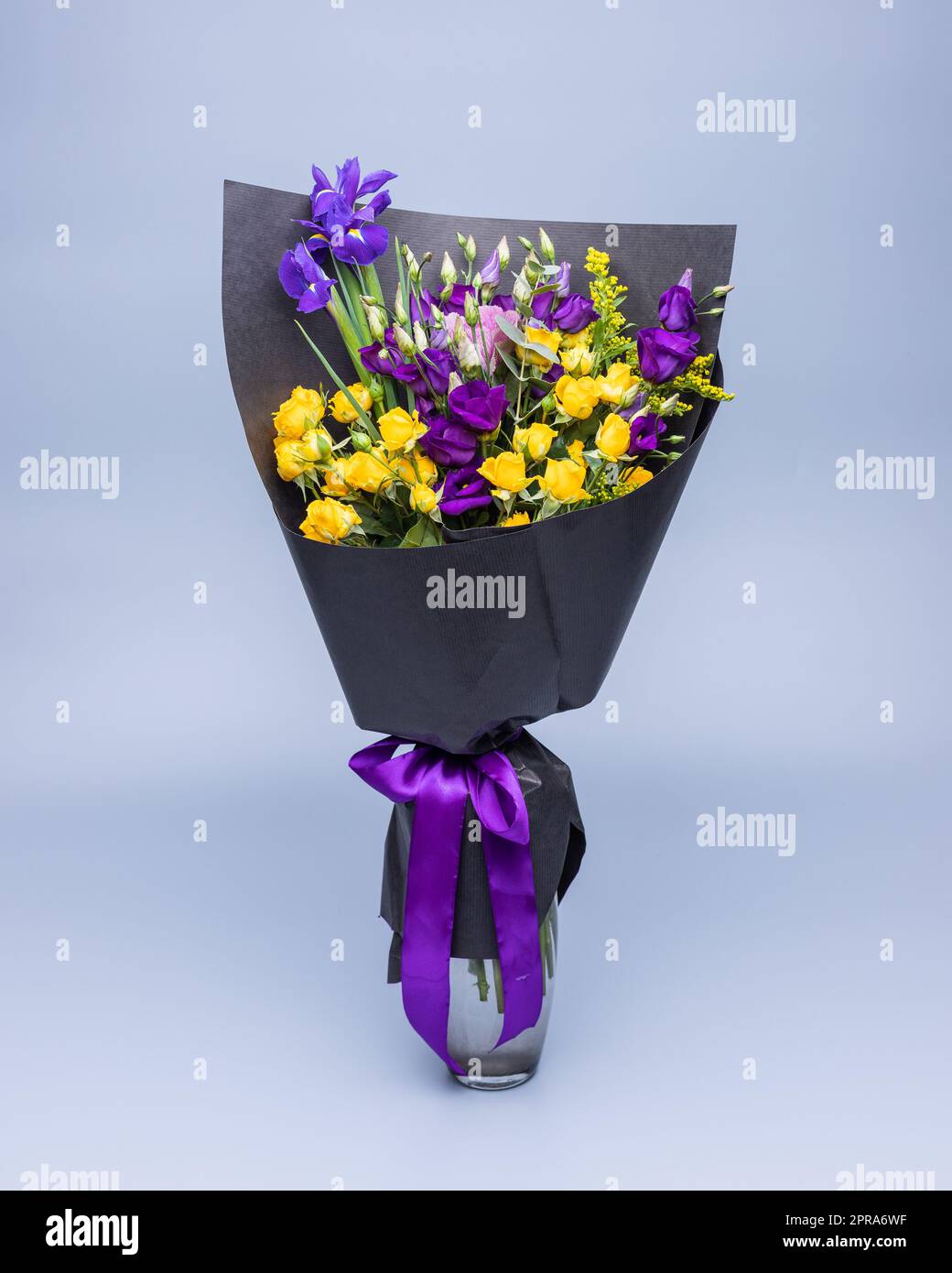 Elegante bouquet di fiori gialli e viola avvolti in carta nera su sfondo blu. Foto Stock