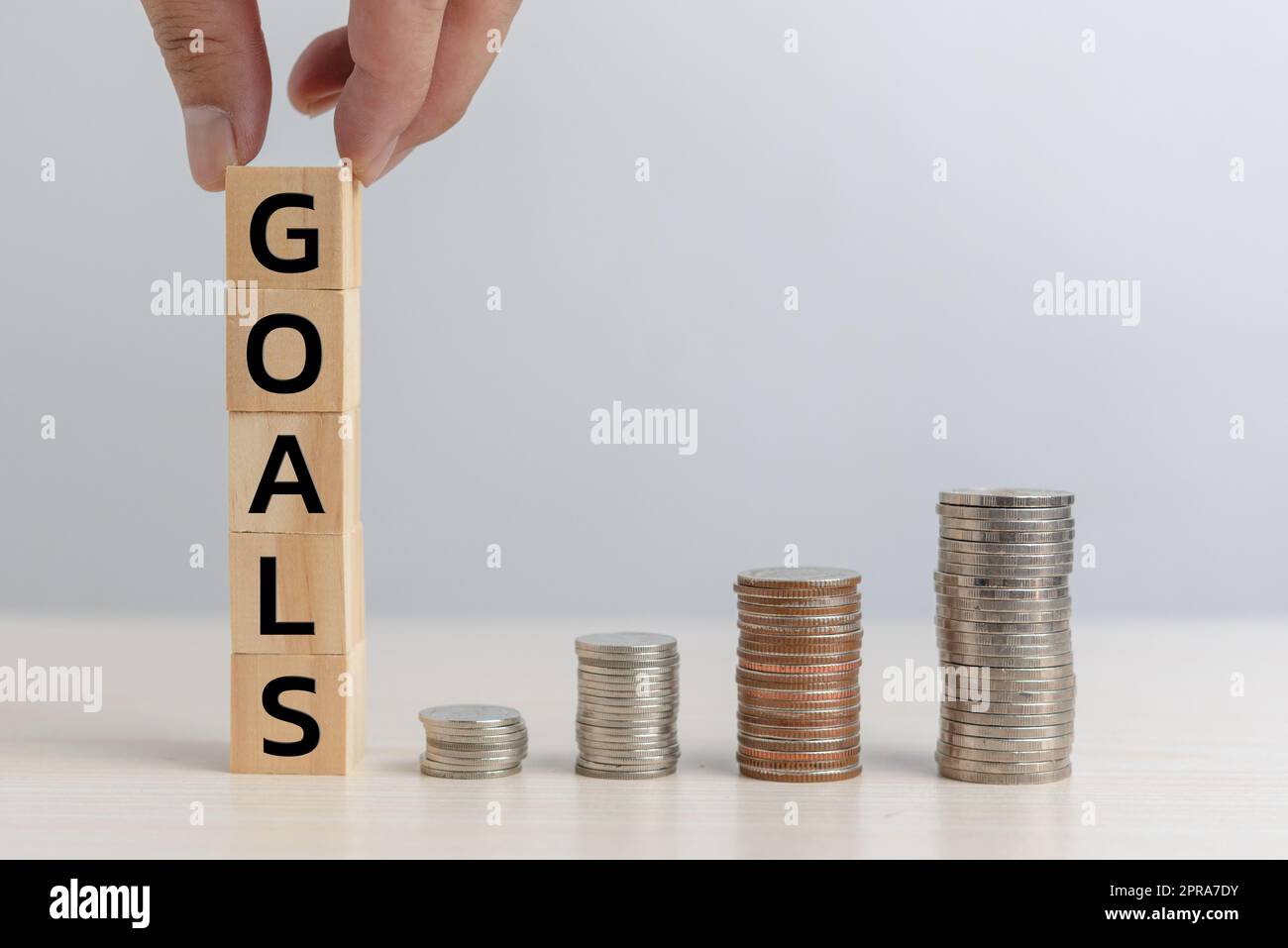 Mano tiene in mano gli obiettivi del blocco del cubo di legno e moneta gli investimenti finanziari di economia di affari e la contabilità di gestione sul concetto della tabella. Foto Stock
