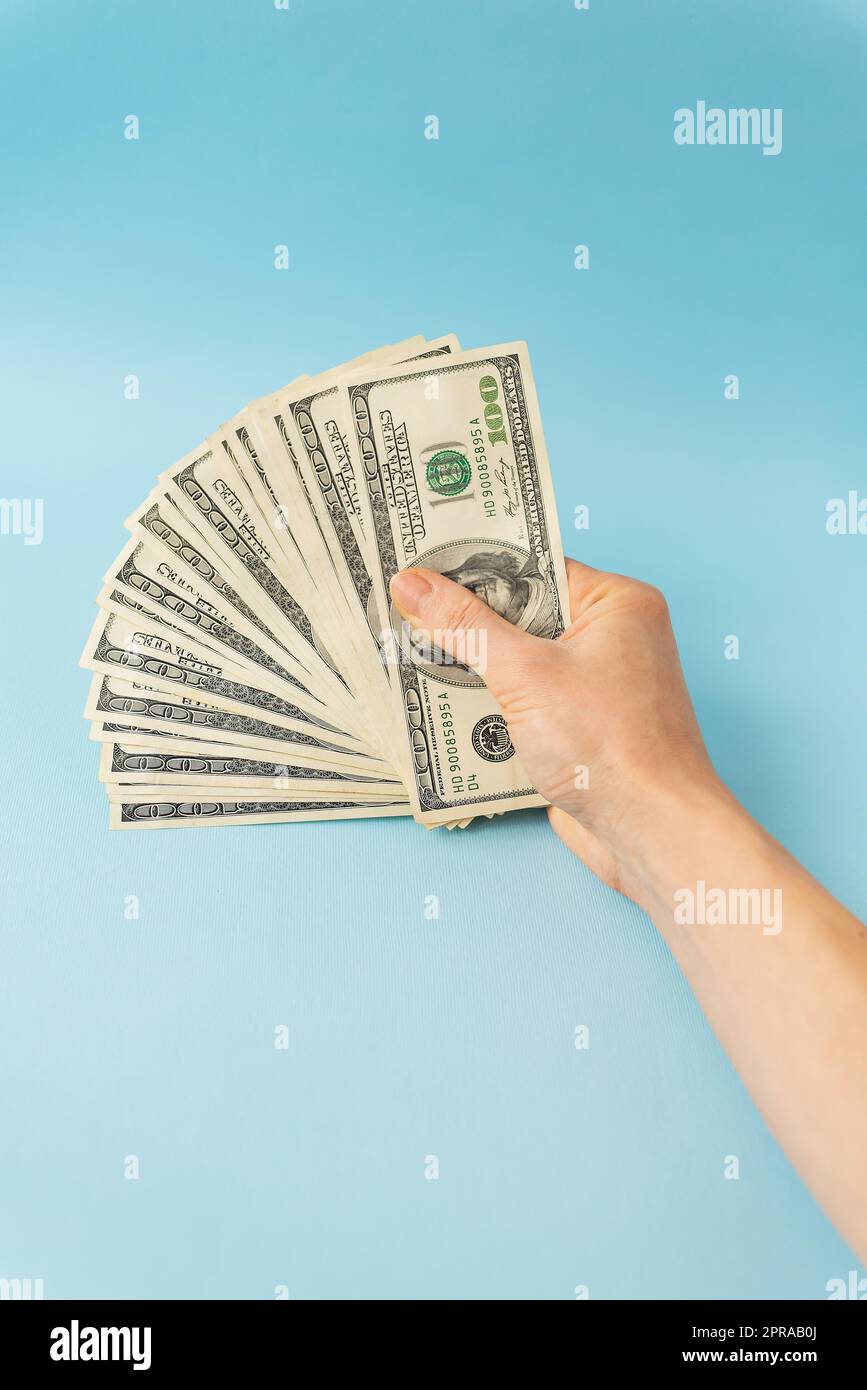 Mani femminili con banconote da 100 dollari isolate su sfondo blu. Foto Stock