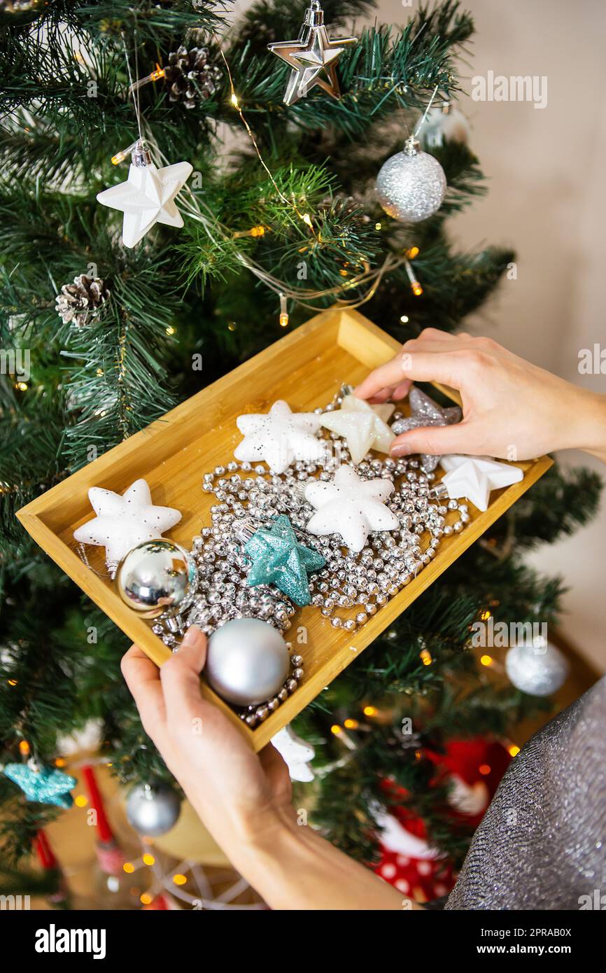 Ragazza che tiene un vassoio di legno con giocattoli di natale e decora un albero di natale, si prepara per Capodanno e natale. Foto Stock