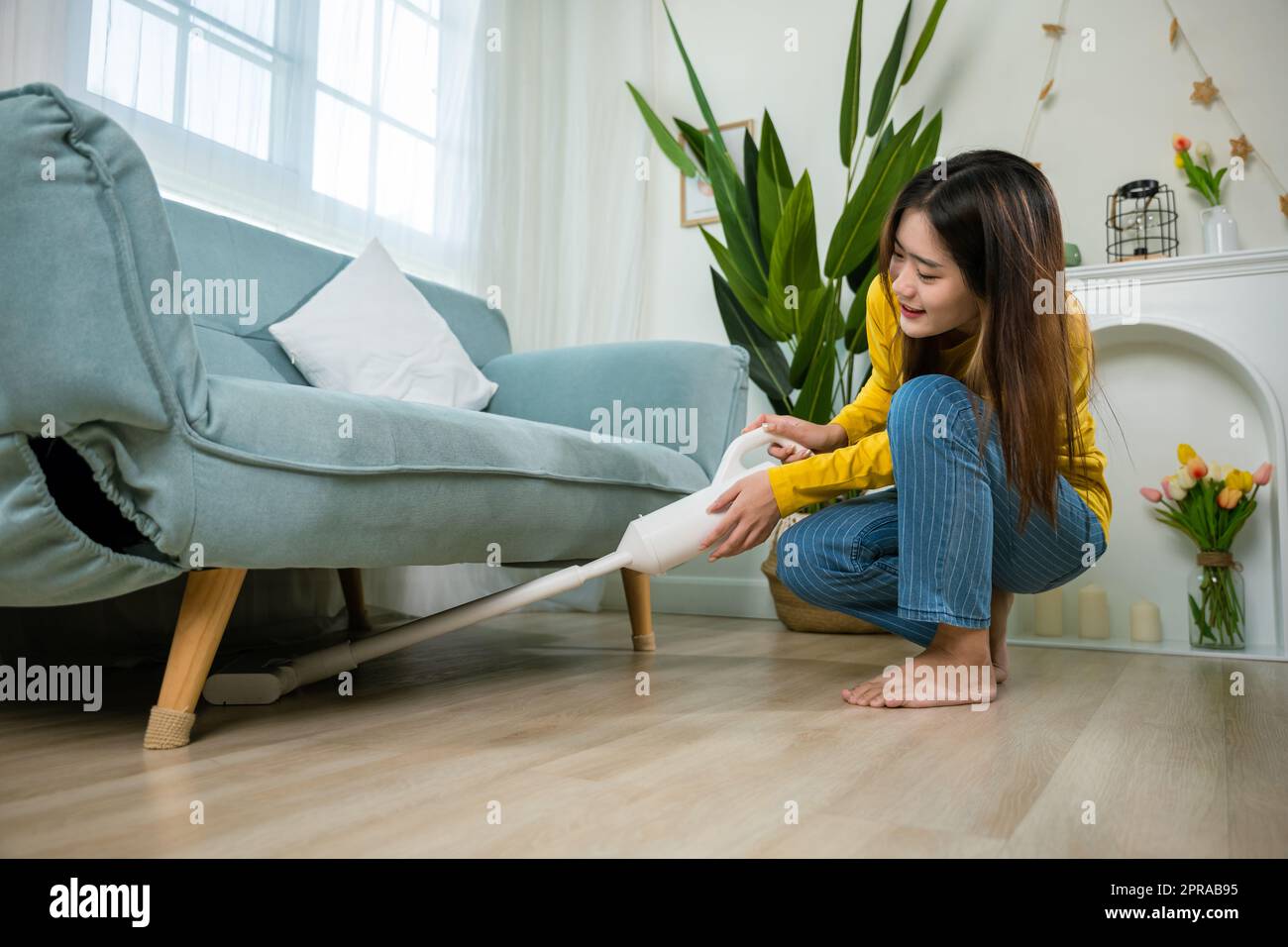 Casalinga donna polvere pulizia pavimento sotto divano o divano mobili con aspirapolvere Foto Stock