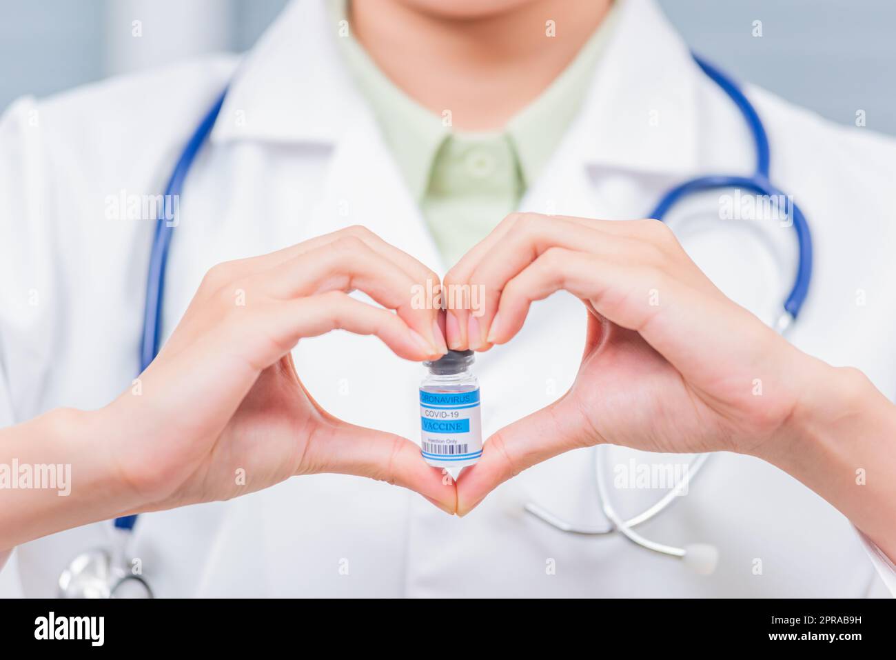 donna medico sorridere formando un cuore con le sue mani segno cuore dito mostrando una fiala di vetro di vaccino coronavirus Foto Stock