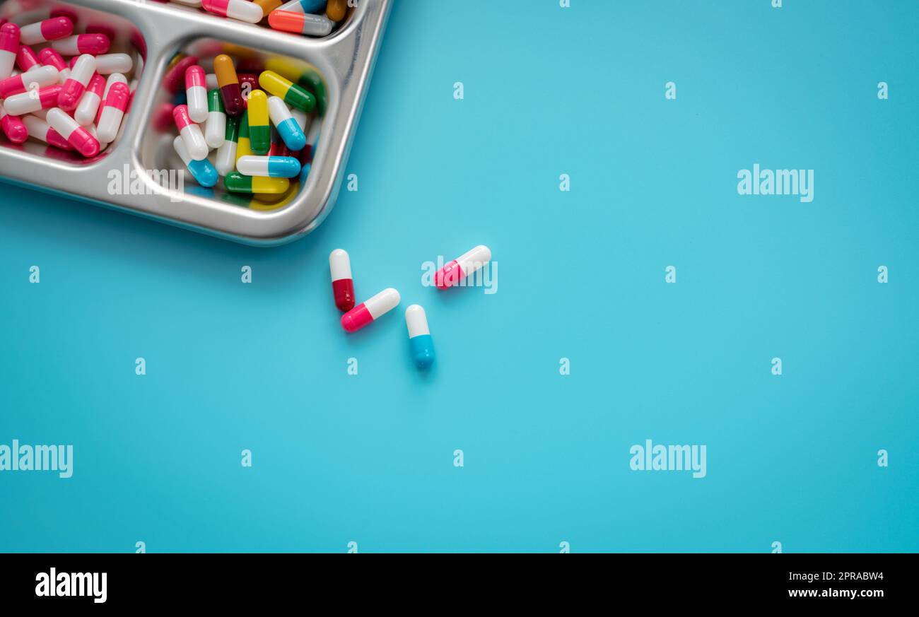 Capsule pillole multicolore in vassoio in acciaio inox e su sfondo blu. Banner della farmacia. Industria farmaceutica. Farmaceutica. Farmaci prescritti. Settore medico e sanitario. Problemi legati alla droga. Foto Stock