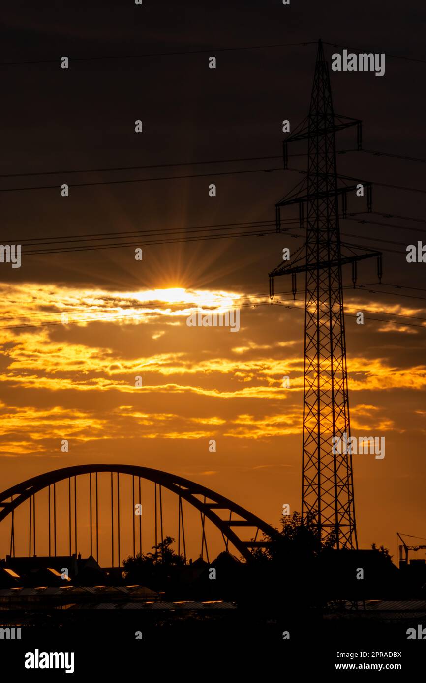 Il cielo dorato con i raggi del sole e il bagliore delle lenti mostra energia solare con la silhouette del pilone della torre elettrica nel tramonto dorato e il cielo arancione per un'energia sostenibile o fonti rinnovabili dal tramonto all'alba Foto Stock