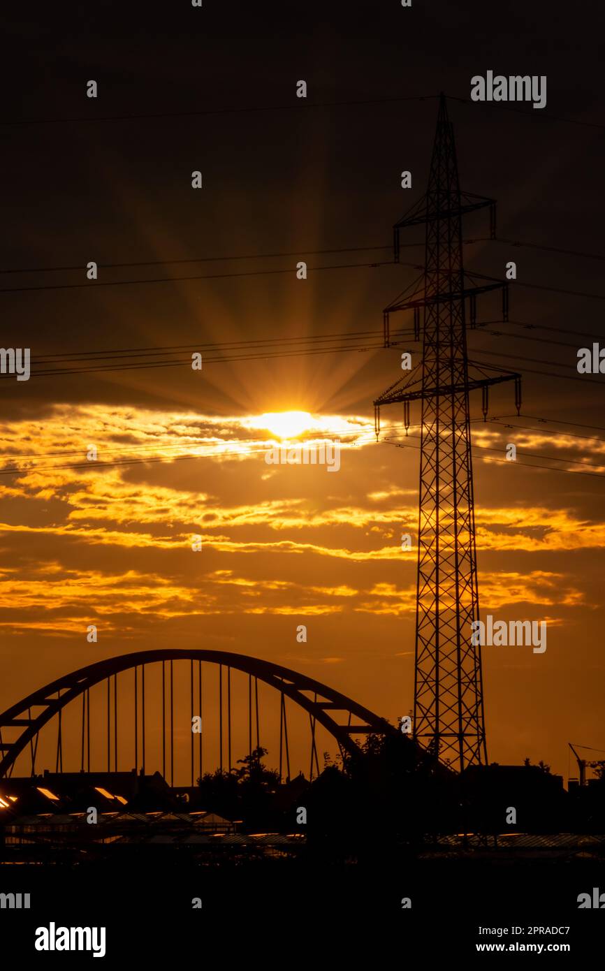 Il cielo dorato con i raggi del sole e il bagliore delle lenti mostra energia solare con la silhouette del pilone della torre elettrica nel tramonto dorato e il cielo arancione per un'energia sostenibile o fonti rinnovabili dal tramonto all'alba Foto Stock