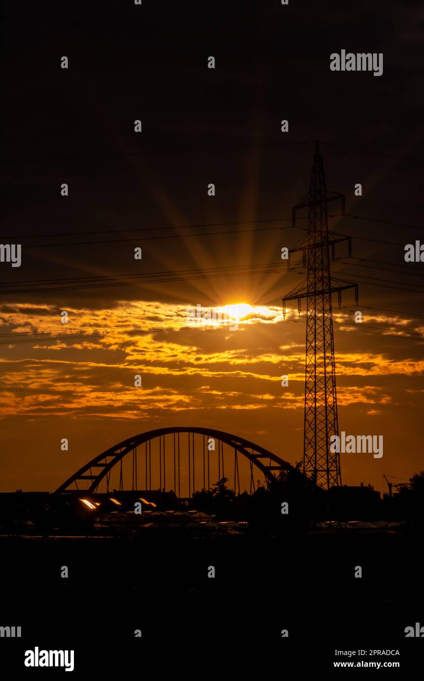 Il cielo dorato con i raggi del sole e il bagliore delle lenti mostra energia solare con la silhouette del pilone della torre elettrica nel tramonto dorato e il cielo arancione per un'energia sostenibile o fonti rinnovabili dal tramonto all'alba Foto Stock