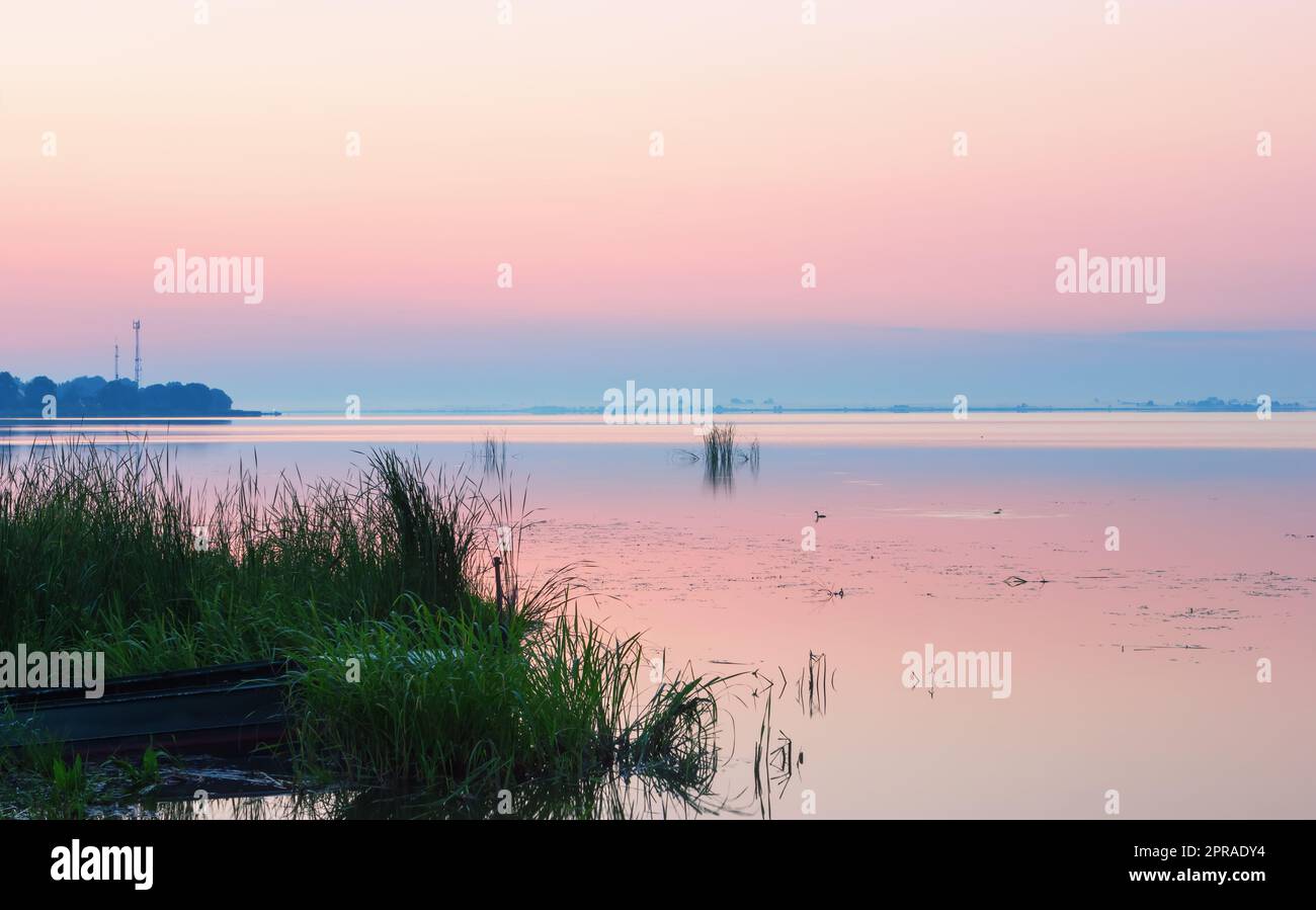 Gentle Pink Dawn sopra l'orizzonte blu di un lago calmo Foto Stock