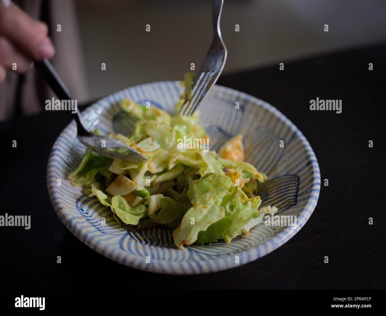 Donna che mescola deliziosi ingredienti per insalata alimentare con cucchiai in cucina Foto Stock