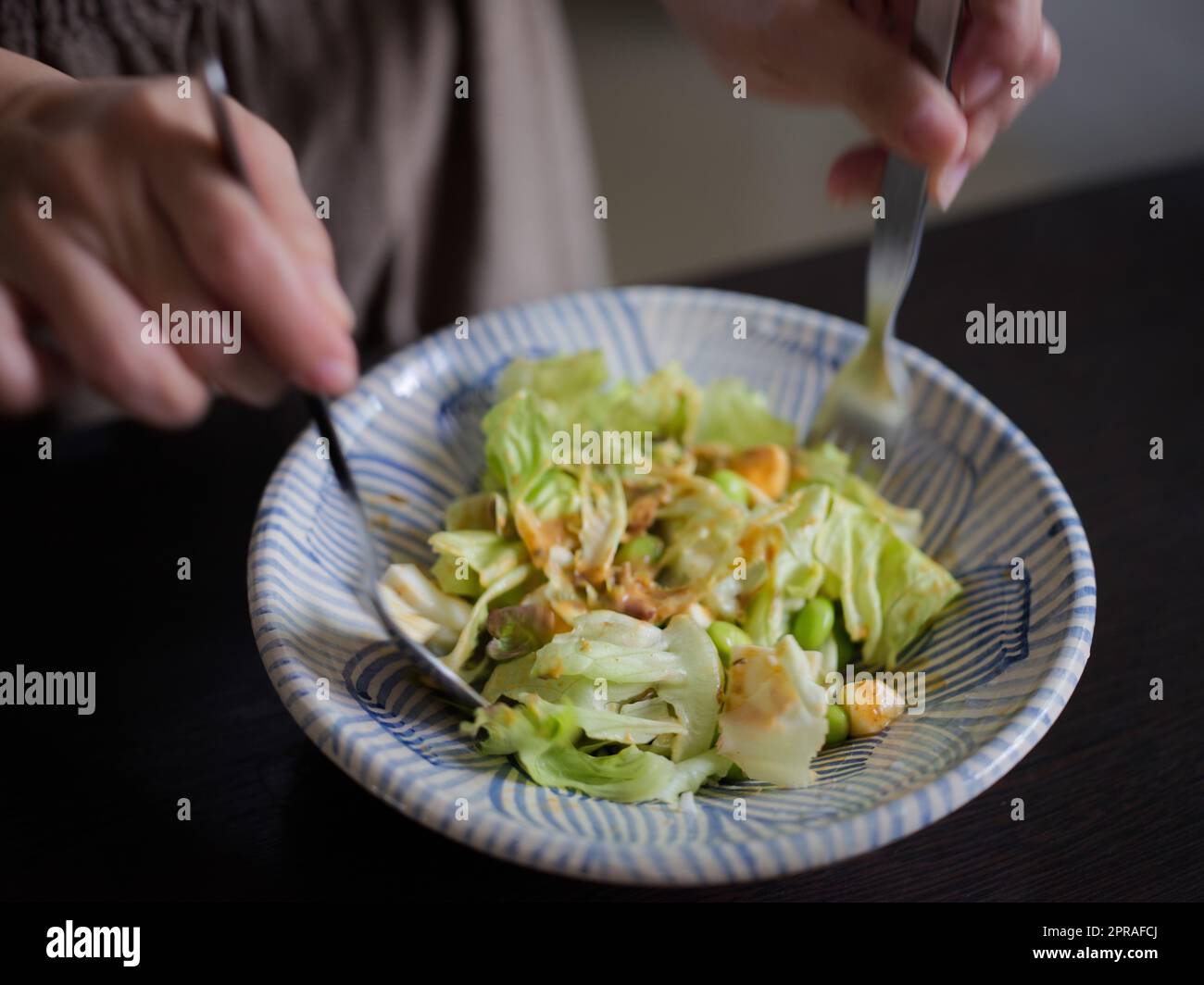 Donna che mescola deliziosi ingredienti per insalata alimentare con cucchiai in cucina Foto Stock
