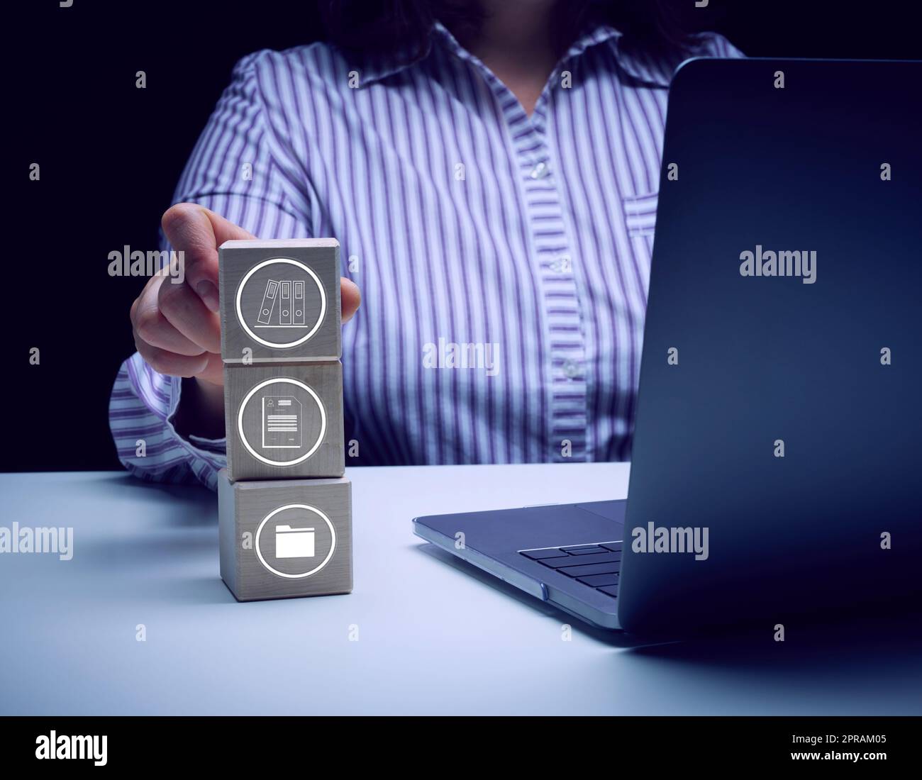 Una donna siede a un tavolo con un notebook e tiene in mano cubi di legno con icone. Foto Stock