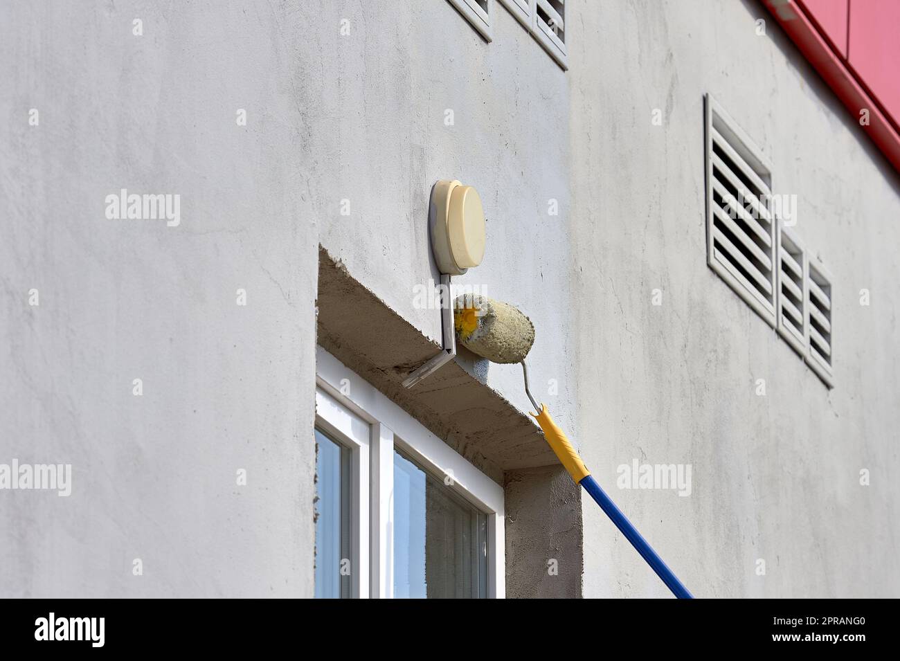 dipingere il muro della strada con un rullo di vernice grigia Foto Stock