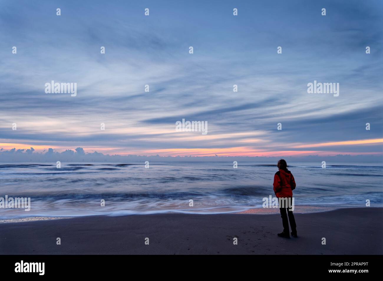 Una donna in piedi vicino all'oceano dopo il tramonto. Esposizione lunga. Riserva dune dell'Olanda settentrionale, Egmond aan Zee, Paesi Bassi. Foto Stock