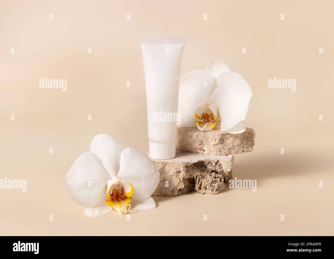 Tubo di crema bianco vicino a fiore di orchidea bianco su giallo chiaro, Mockup. Prodotto per la cura della pelle Foto Stock