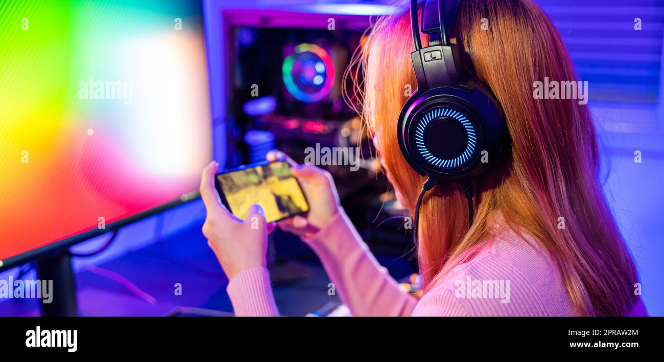 Donna asiatica in diretta streaming lei gioca ai videogiochi tramite smartphone nel salotto delle luci al neon di casa Foto Stock