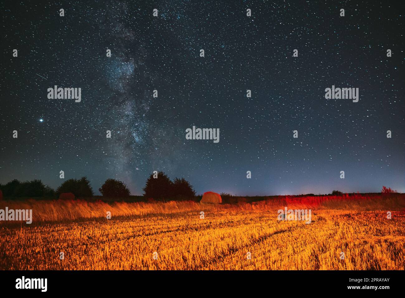 La via Lattea Galaxy in Night Starry Sky sopra Haystack nel campo agricolo estivo. Stelle notturne sopra il paesaggio rurale con Hay Bale dopo la vendemmia. Concetto agricolo Foto Stock