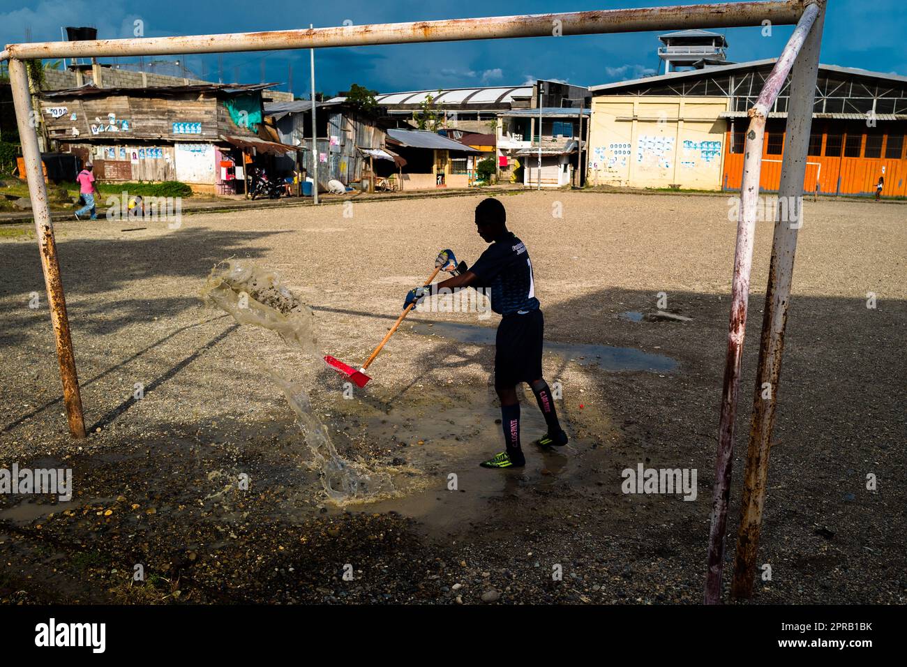 Un giovane portiere afro-colombiano rimuove una pozza d'acqua prima di giocare una partita di calcio su un campo da gioco sporco a Quibdó, Chocó, Colombia. Foto Stock