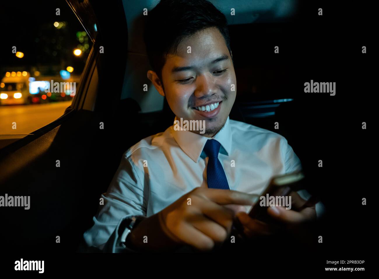 Uomo d'affari che utilizza lo smartphone sul retro dell'auto vicino al finestrino di notte Foto Stock