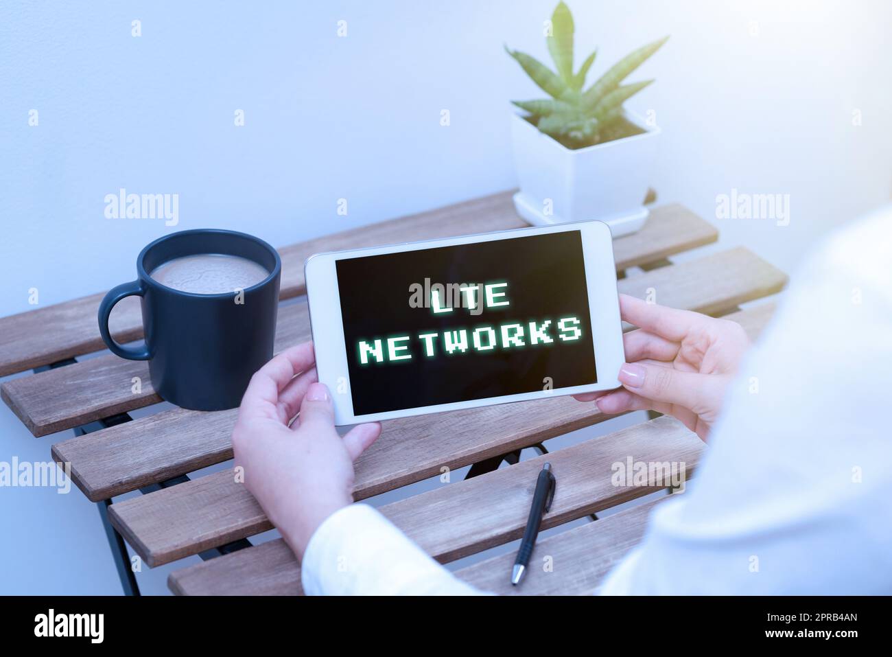 Reti LTE con didascalia concettuale. Word per la connessione di rete più veloce disponibile per le comunicazioni wireless donna che detiene un tablet con dati recenti sul tavolo con caffè, penna e impianto Foto Stock