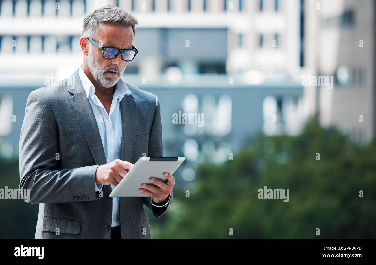 Rimando al lavoro da qualsiasi luogo. Un uomo d'affari maturo che utilizza un tablet su un background urbano. Foto Stock