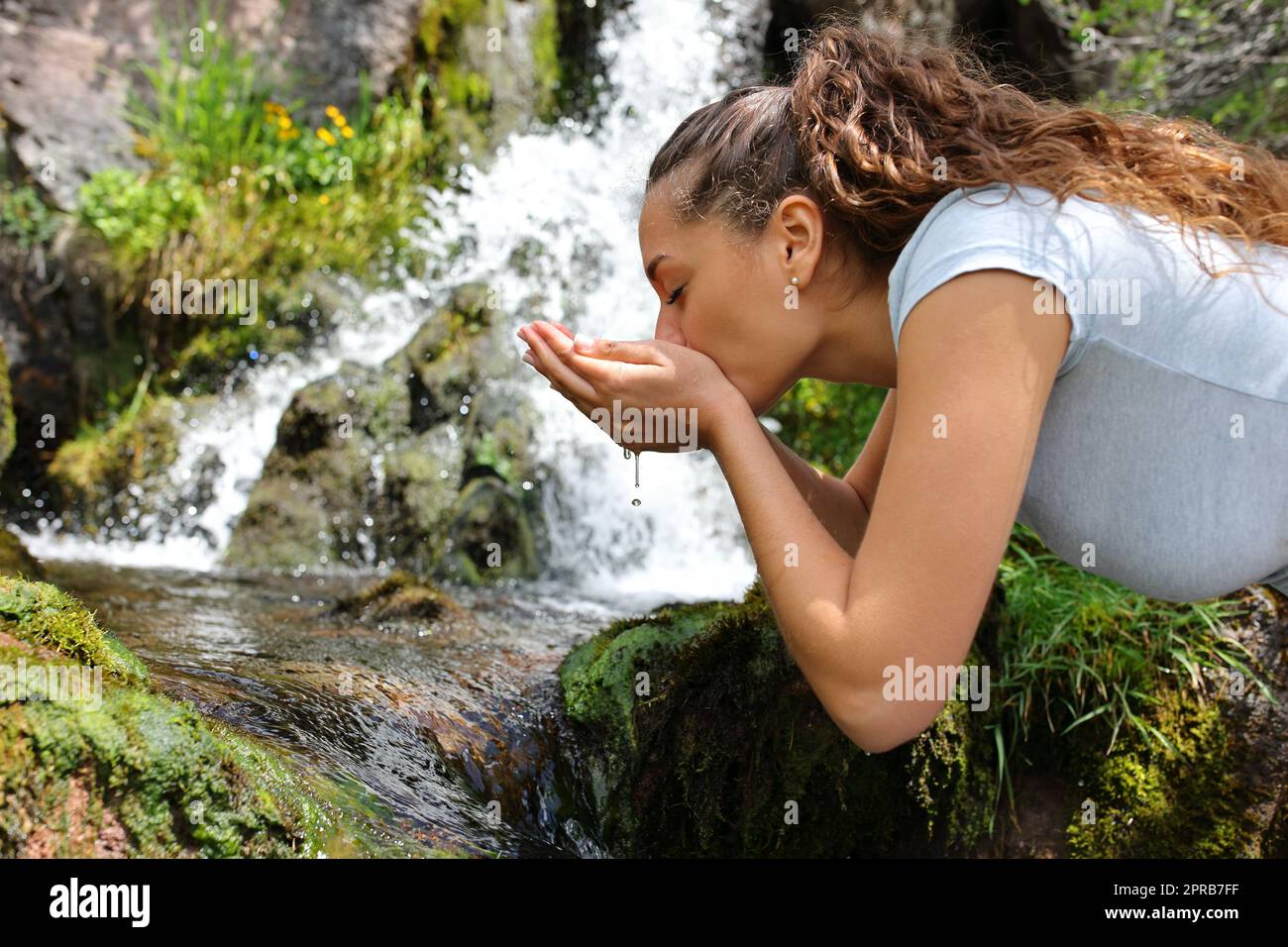 Donna che beve acqua dal fiume in montagna Foto Stock