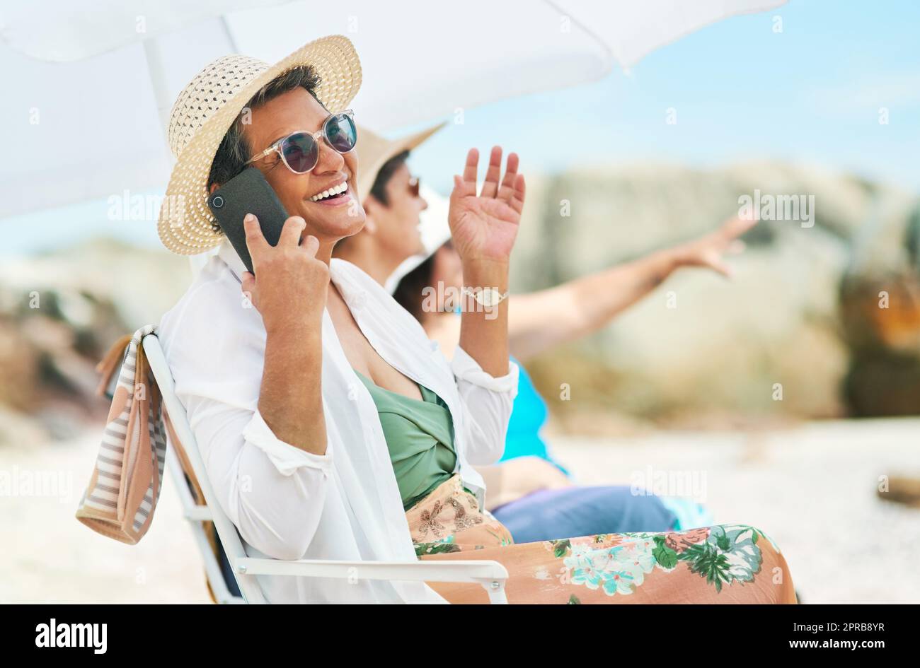 Abbiamo fatto la giornata migliore qui fuori: Una donna matura seduta da sola e con gli amici che usavano il cellulare durante una giornata in spiaggia. Foto Stock