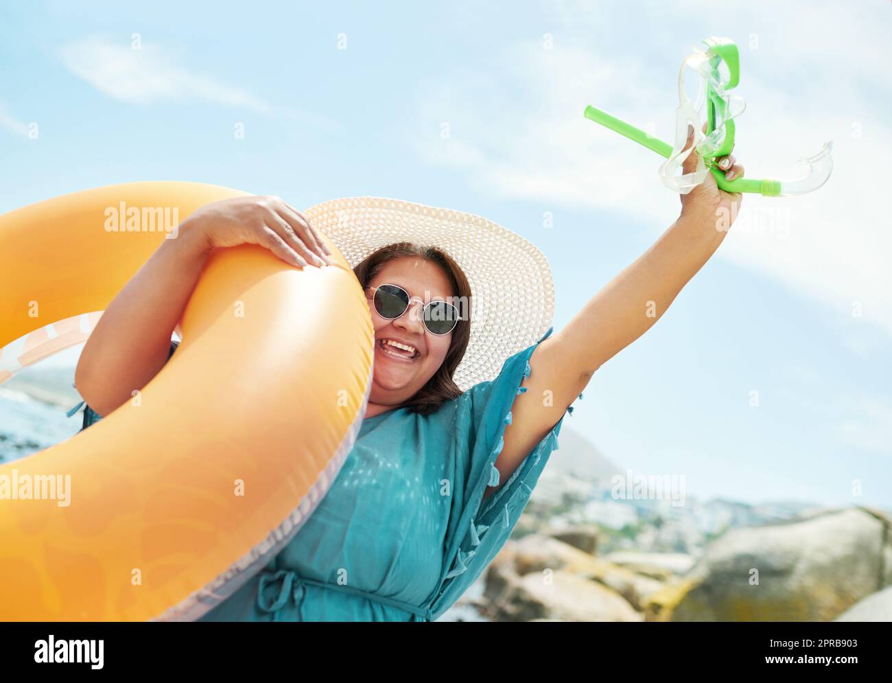 Gareggia in acqua. Una donna matura in piedi e in possesso di una piscina gonfiabile e snorkeling durante una giornata sulla spiaggia. Foto Stock