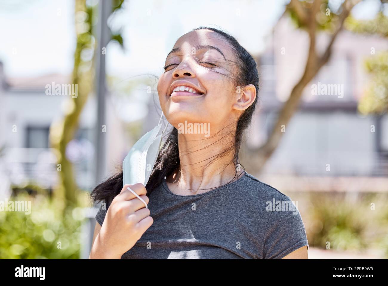 Si sente bene a riempire i miei polmoni di aria fresca. Una giovane donna che prende la sua maschera facciale dopo aver corso per una corsa all'aperto. Foto Stock