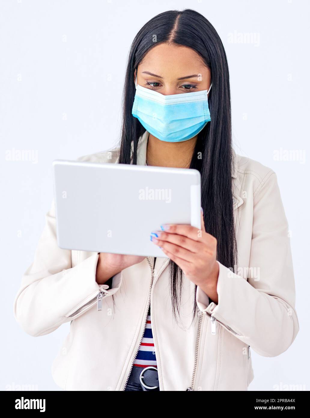 Sfogliare gli aggiornamenti in tempo reale sulla pandemia. Studio girato di una giovane donna che indossa una maschera e usando un tablet digitale su sfondo bianco. Foto Stock